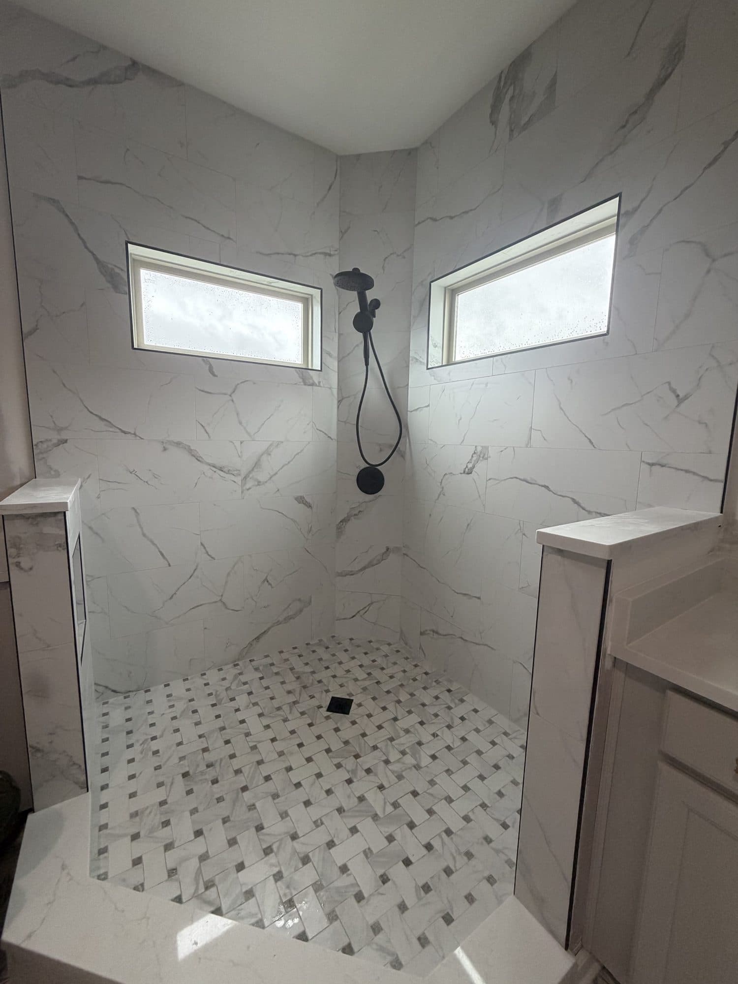 Marble-look porcelain walk-in shower with basketweave mosaic floor and black fixtures by Remodel CLT, Charlotte NC