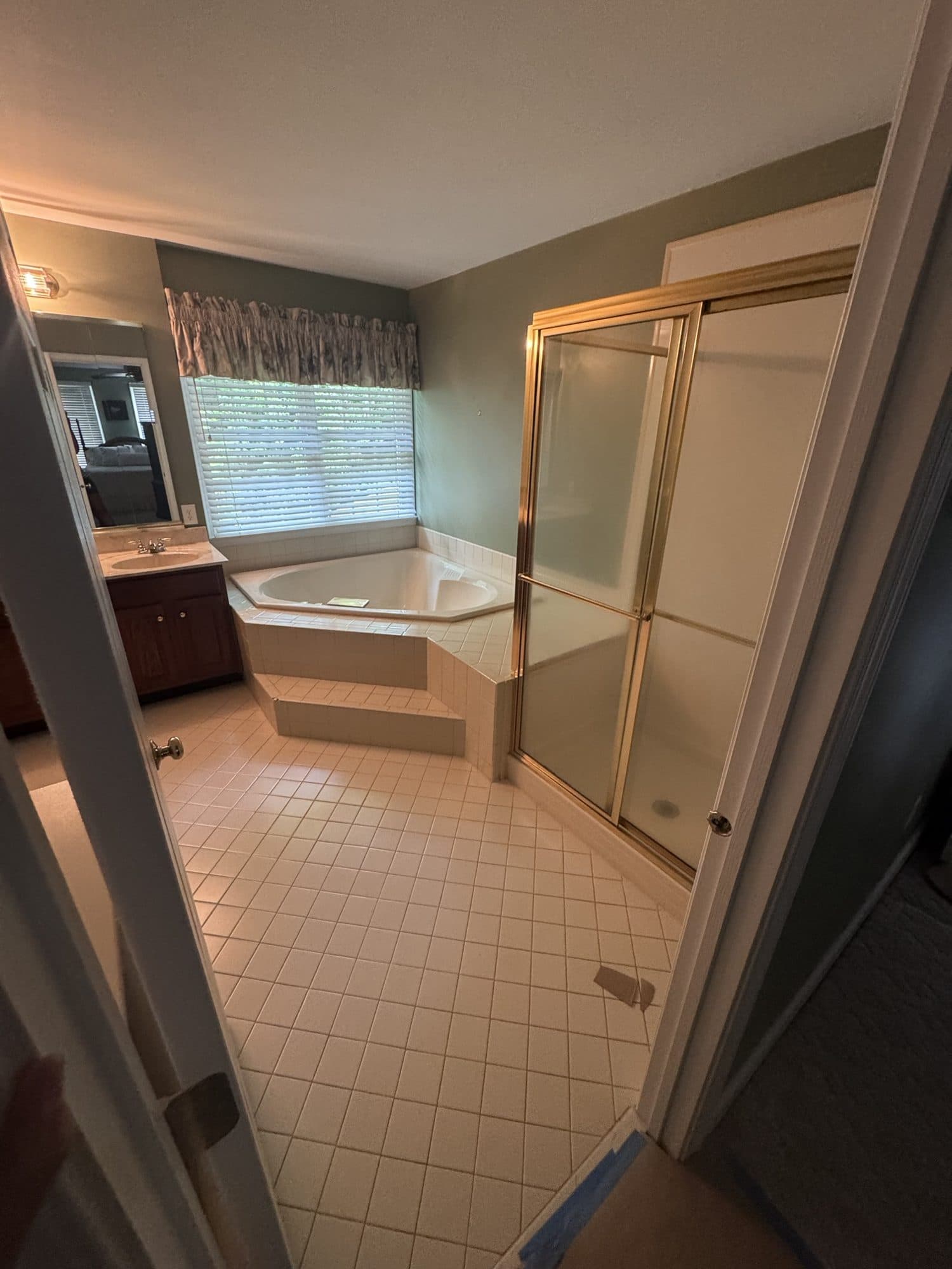 Before: 1990s primary bathroom with corner jetted tub, gold-framed shower and small diamond tile floor in Matthews, NC