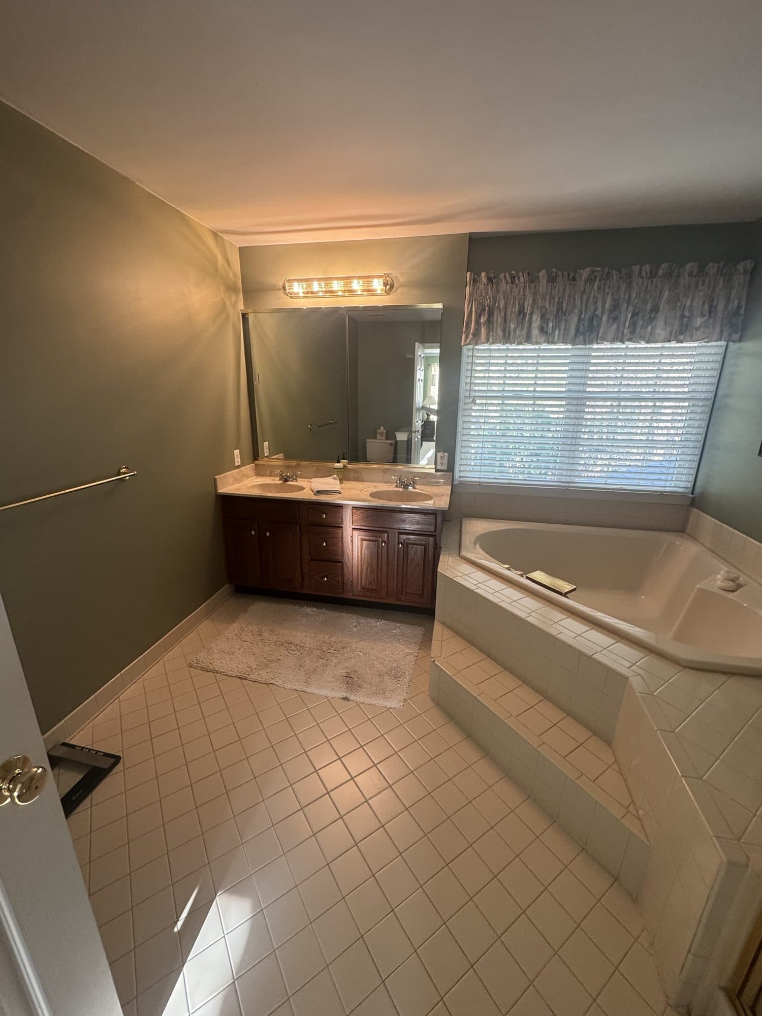 Before: oak double vanity with cultured marble top and corner tub in a Matthews, NC primary bathroom