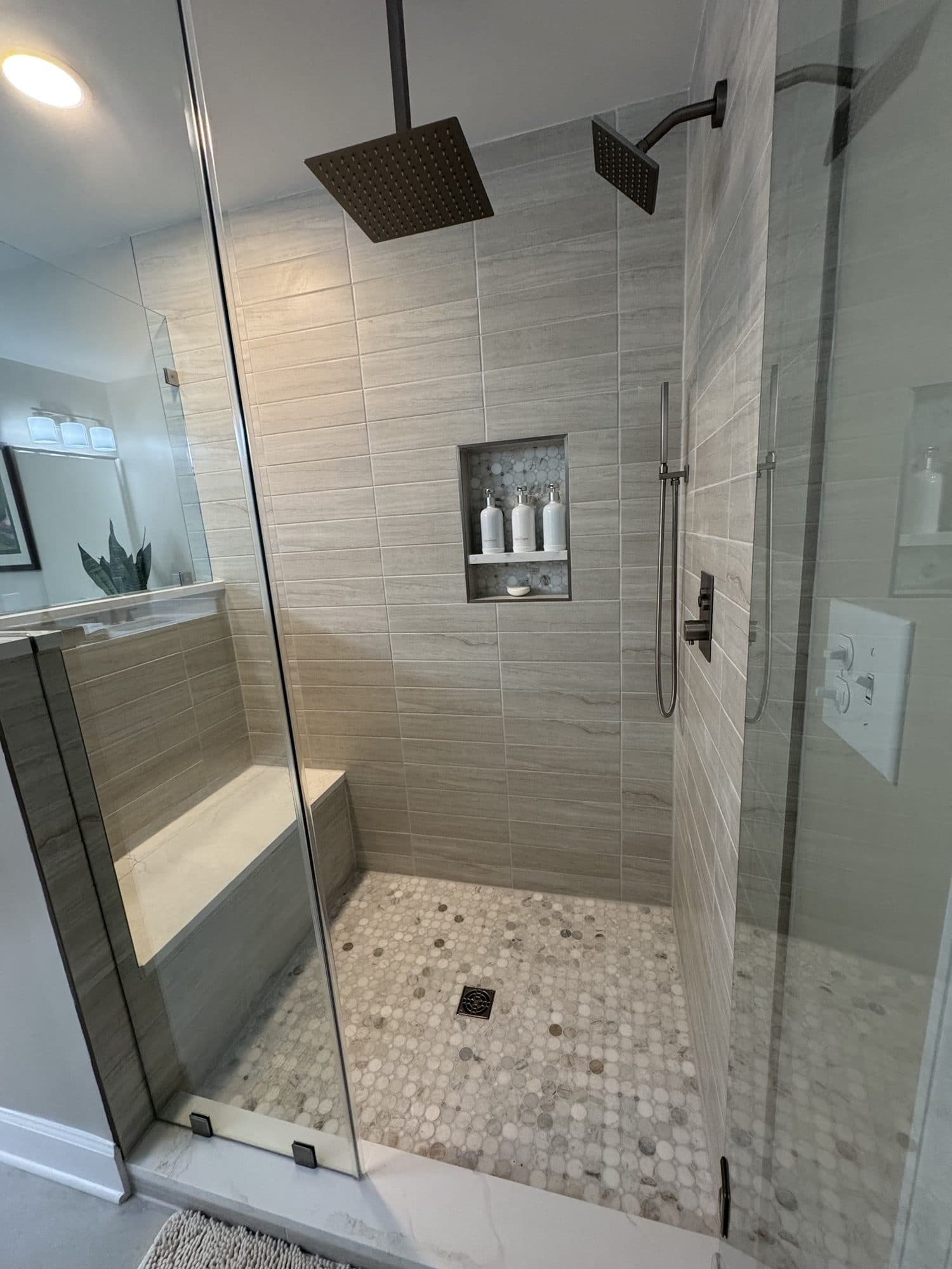 Walk-in shower with ceiling rain head, wall shower, quartz bench, marble mosaic niche and circle marble floor in Matthews, NC