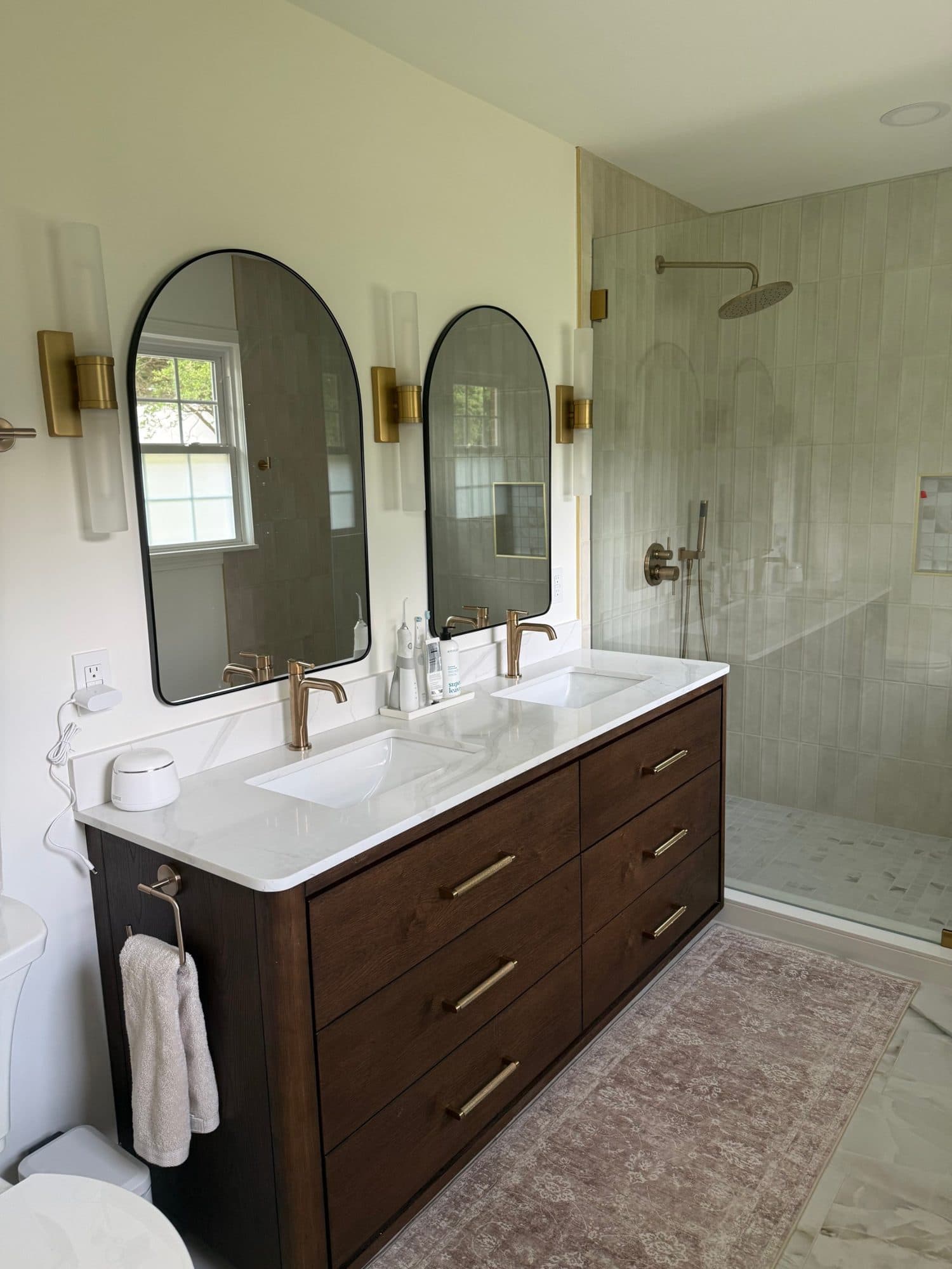 Custom dark wood double vanity with arched mirrors and brushed brass sconces in a SouthPark, Charlotte primary bath