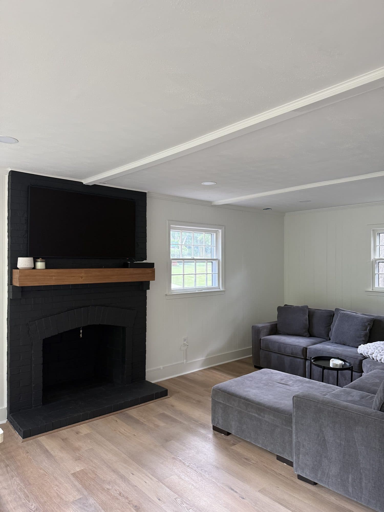 Den refresh in SouthPark, Charlotte: black painted brick fireplace, wood mantel, painted paneling and new LVP floors