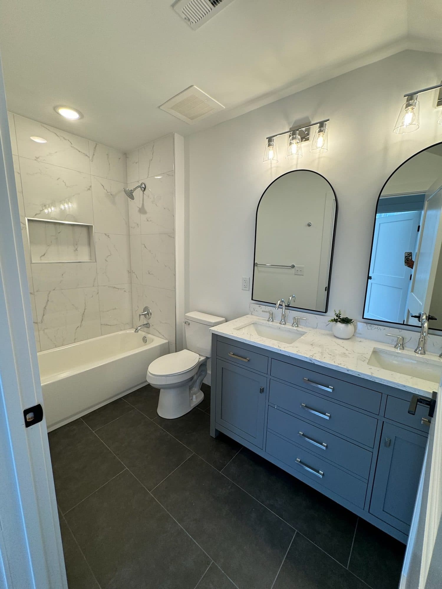 Bathroom with gray double vanity, quartz top, arched mirrors and marble-look tub surround at The Arches, Charlotte