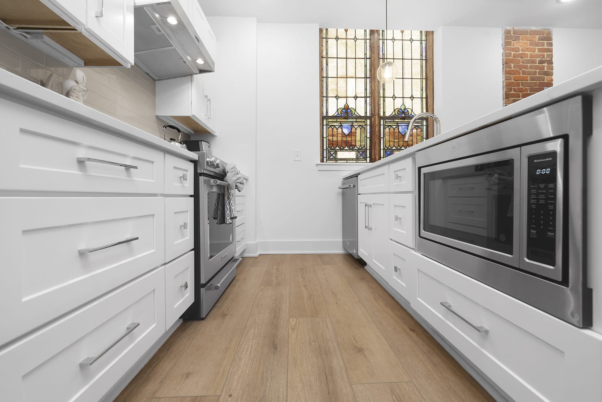 Galley kitchen with original stained glass and exposed brick at The Arches church conversion, Wesley Heights, Charlotte