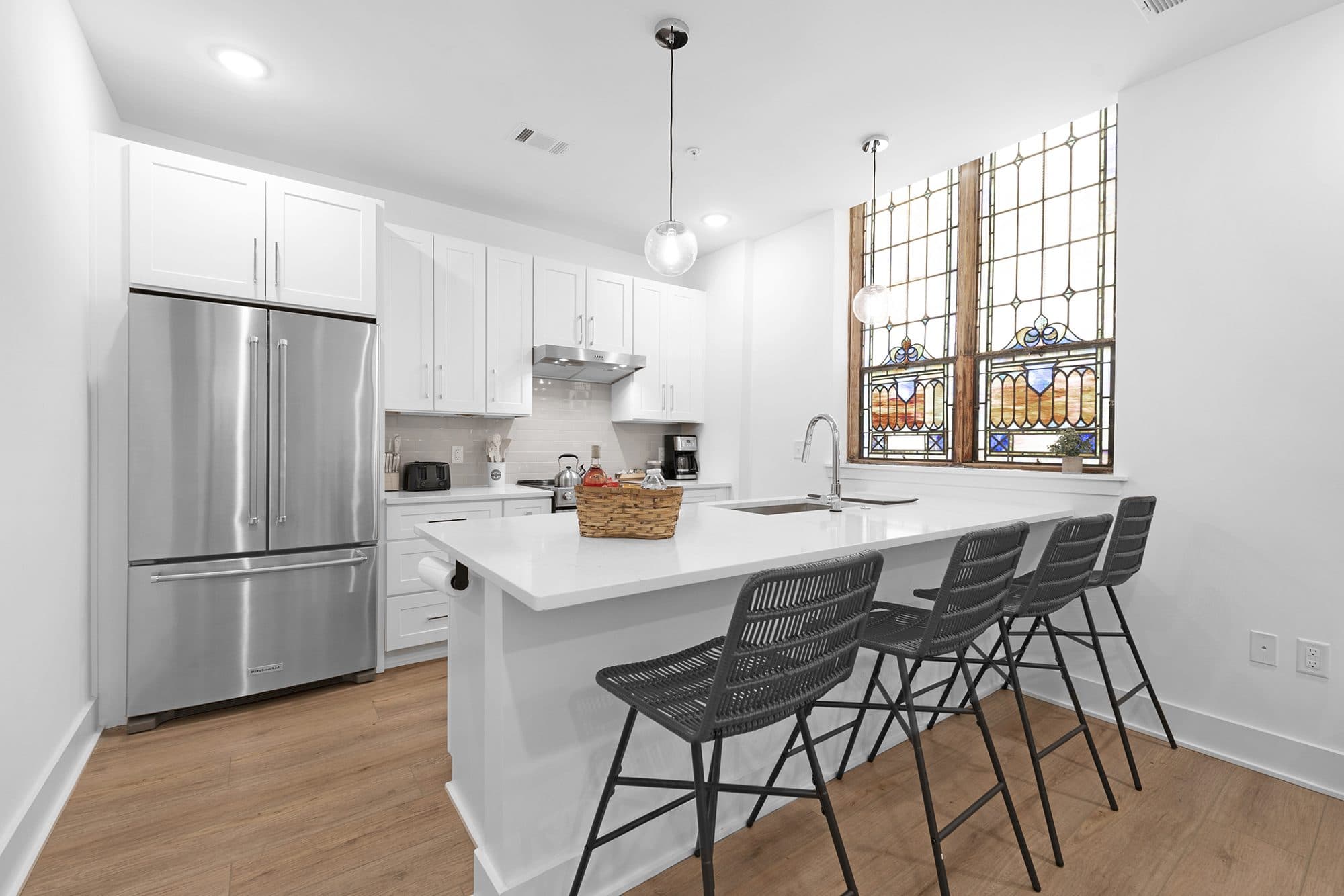 Kitchen at The Arches in Wesley Heights, Charlotte: white shaker cabinets, quartz peninsula and original stained-glass windows