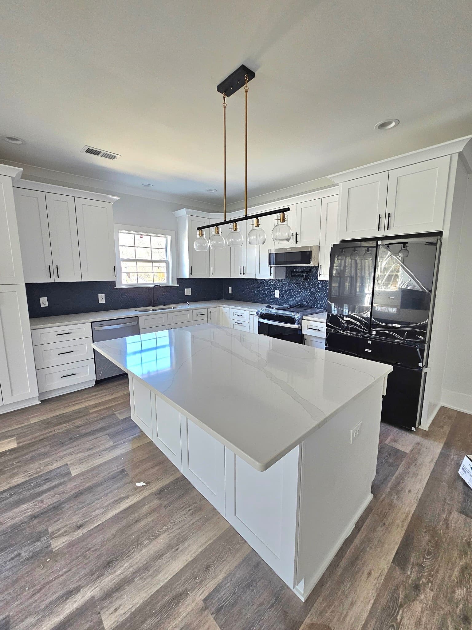 Kitchen renovation in Charlotte with white shaker cabinets, black backsplash, and gold pendants.